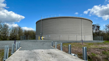 image of a large concrete water reservoir with blue sky, clouds and trees
